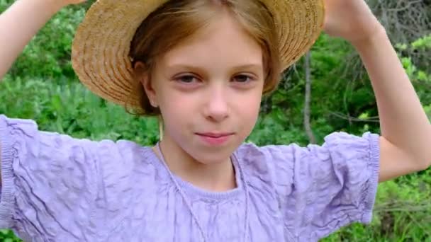 Ένα Κορίτσι Ψάθινο Καπέλο Κοιτάζει Την Κάμερα Ενάντια Στην Πράσινη — Αρχείο Βίντεο