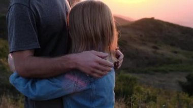 Babam kızlarını okşar, başını dağların arka planına ve günbatımının gökyüzüne yaslar. Yüksek kalite 4k görüntü