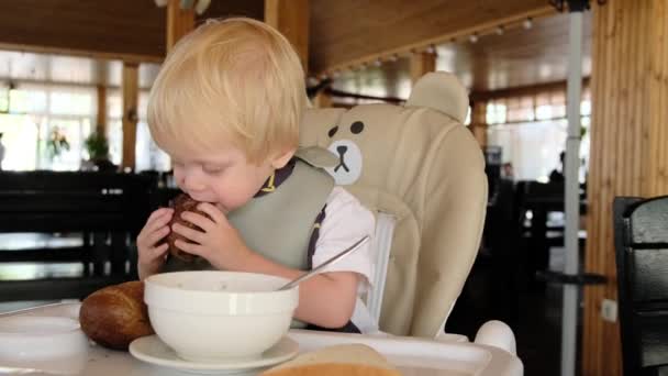 Uma Criança Senta Uma Cadeira Alta Restaurante Come Grande Pedaço — Vídeo de Stock