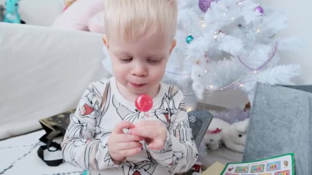 一个可爱的小男孩在一棵白色的圣诞树上咬着棒棒糖 高质量的4K镜头 — 图库视频影像