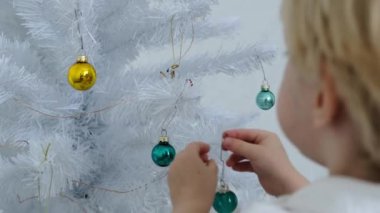 Bir çocuk beyaz bir odada Noel ağacı süslüyor. Yüksek kalite 4k görüntü