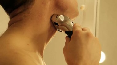 Bir adam aynanın önünde dikilirken elektrikli jiletle tıraş olur. Yüksek kalite 4k görüntü