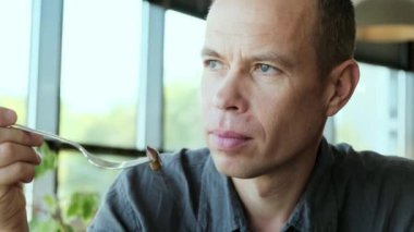 Düşünceli görünüşlü bir adam bir restoranda öğle yemeği yiyor ve pencereden dışarı bakıyor. Yüksek kalite 4k görüntü