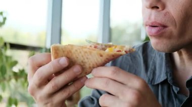 Gri tişörtlü bir adam restoranda bir masada oturmuş bir dilim pizzanın tadını çıkarıyor. Yemek reklamları, restoran reklamları ve günlük yemek içeriği için ideal 4K video. Yüksek kalite 4k görüntü