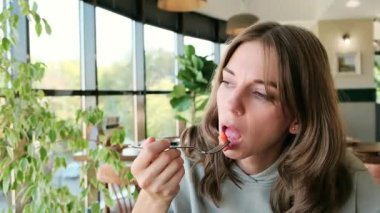 Genç, güzel bir kadın bir restoranda çataldan ağzına bir parça çilek koyar. Yemek reklamları, restoran reklamları ve yaşam tarzı içeriği için mükemmel bir 4K videosu. Yüksek kalite 4k görüntü