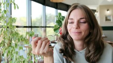 Güzel bir kadın çatalın üzerinde bir parça tatlı dener ve kameraya zevkle bakar. Yemek reklamları, tatlı reklamları ve mutfak malzemeleri için mükemmel bir 4K videosu. Yüksek kalite 4k görüntü