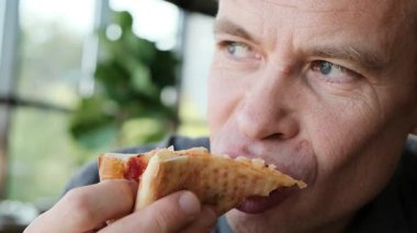 Restoranda bir adam pizzadan bir ısırık alır ve ona dikkatlice bakar. Yemek reklamları, restoran tanıtımları ve mutfak içeriği için ideal 4K video. Yüksek kalite 4k görüntü