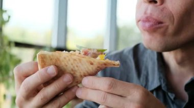 Restoranda bir adam bir dilim pizza tutuyor ve dikkatlice ısırılmış bir parça çiğniyor. Yemek reklamları, restoran tanıtımları ve mutfak içeriği için mükemmel bir 4K videosu. Yüksek kalite 4k görüntü