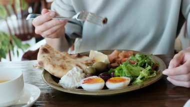 Lokantada lezzetli bir kahvaltıyı yakından çekerken bir kız çatalını alır ve yemeğinin tadını çıkarmaya başlar. Yemek reklamları, restoran tanıtımları ve sabah yemeği içeriği için video. Yüksek kalite 4k görüntü