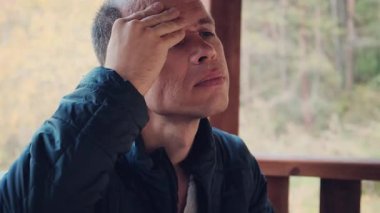 Orta yaşlı bir adam, şiddetli baş ağrısı belirtileri gösteren acı dolu bir ifadeyle kafasına dokunuyor. Sağlık, stres ve tıbbi içerik için mükemmel bir 4K videosu. Yüksek kalite 4k görüntü
