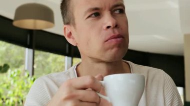 Orta yaşlı beyaz bir adam, elinde bir fincan kahveyle bir restoranda oturur ve yemek çiğnerken dikkatle etrafa bakar. Kafe reklamları için mükemmel 4K video. Yüksek kalite 4k görüntü