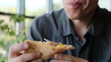 Gri tişörtlü bir adam restoranda bir masada oturmuş bir dilim pizzanın tadını çıkarıyor. Yemek reklamları, restoran reklamları ve günlük yemek içeriği için ideal 4K video. Yüksek kalite 4k görüntü