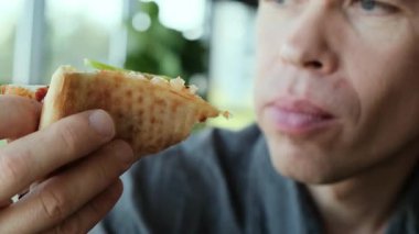 Restoranda bir adam bir dilim pizza tutuyor ve dikkatlice ısırılmış bir parça çiğniyor. Yemek reklamları, restoran tanıtımları ve mutfak içeriği için mükemmel bir 4K videosu. Yüksek kalite 4k görüntü