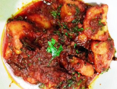 Bir tabakta taze kişniş ile süslenmiş kırmızı domates sosuna bulanmış patates parçaları yer alıyor. Canlı renkler ve görünen baharatlar lezzetli ve baharatlı bir hazırlık olduğunu gösteriyor..