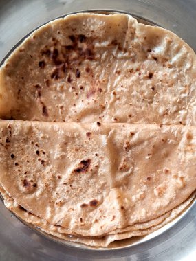 Bir yığın taze pişmiş ekmek, muhtemelen roti, metal bir konteynırda düzgünce düzenlenir. Düz ekmeklerin hafif yanmış bir yüzeyi var. Bu da açık bir ateşte pişirildiklerini gösteriyor..