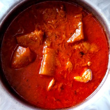 Görünür et ve sebzelerle dolu zengin, kırmızı bir köri bir metal kaseyi doldurur, canlı ve lezzetli bir yemek sergiler. Sos kalın ve baharatlı görünüyor. Yüzeyde biraz yağ parlıyor..