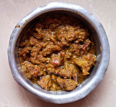 Zengin baharatlı et körisiyle dolu metal bir kase açık renkli bir yüzeyde sergilenir. Tabak sağlıklı görünüyor, tepesinde görünür yağ parlıyor..