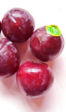 Beş parlak, olgun erik açık bir yüzeye yerleştirilir ve koyu kırmızımsı mor rengini ortaya çıkarır. Eriklerin birinde küçük bir etiket var, markalaşma ya da kaliteyi gösteriyor..