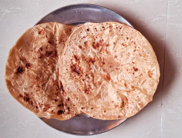 İki gevrek, altın parathas parlak metal bir plaka üzerinde dinleniyor, hafif yanmış benekleri ve pul pul dokularıyla sergileniyorlar. Açık renkli, mermer bir yüzeye yerleştirilirler..