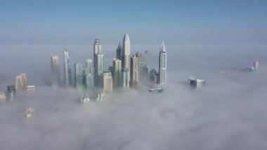 Dubai şehri yoğun bir sis altında. Hava görüntüsü. Açığa vur. Bulutlardan çıkıp gökdelenleri gösteren İHA..