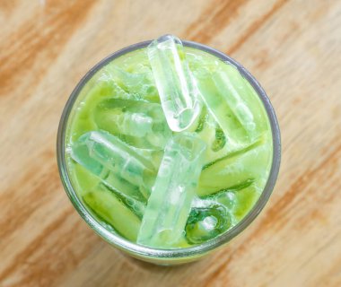 Buzlu kibritli lattenin ya da şeffaf bardaktaki yoğun sütlü yeşil çayın üst görüntüsü bulanık kahverengi ahşap arka plandadır..