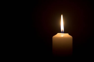 Yanan tek bir mum ya da ışık, kilisedeki siyah ya da koyu arkaplanda beyaz bir mum üzerinde Noel, cenaze ya da anma töreni için parlıyor..