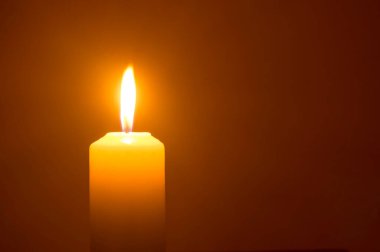Tek bir yanan mum ya da ışık, kilisedeki kırmızı ya da koyu arkaplanda izole edilmiş sarı bir mum üzerinde Noel, cenaze ya da anma töreni için parlıyor..