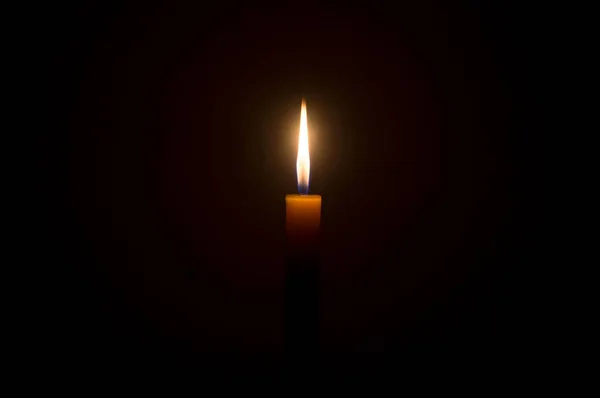 単一の小さな黄色のろうそくに輝く単一の燃焼ろうそくの炎や光は クリスマス 葬儀や記念サービスのための教会や寺院のテーブルの上に黒または暗い背景に隔離されています — ストック写真