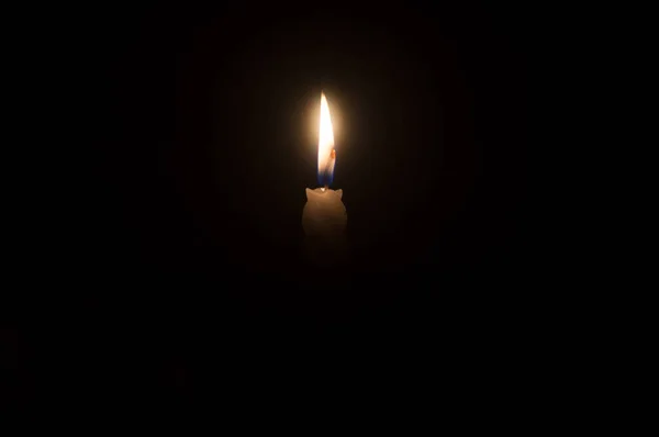 A single burning candle flame or light is glowing on a beautiful spiral white candle on black or dark background on table in church for Christmas, funeral or memorial service with copy space.