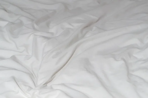 White crumpled or wrinkled bedding sheet or blanket with pattern after guest\'s use was taken in hotel, resort room with copy space. Untidy blanket background texture