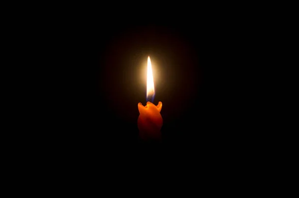 A single burning candle flame or light is glowing on a beautiful spiral orange candle on black or dark background with copy space for adding text on table in church for Christmas, funeral or memorial service.