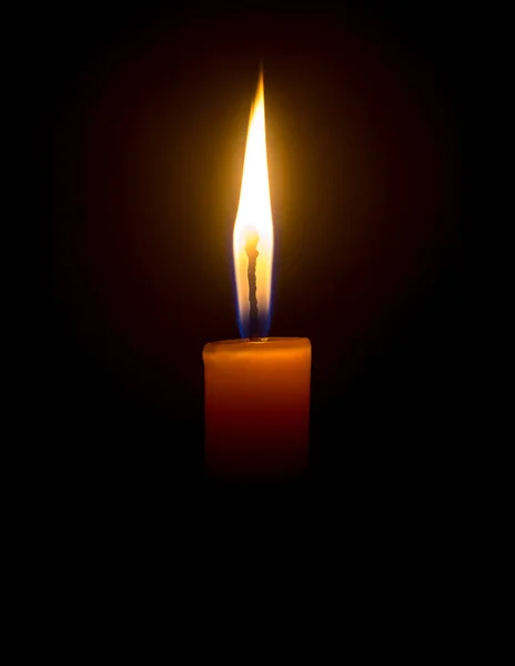 A single burning candle flame or light is glowing on an orange candle on black or dark background on table in church for Christmas, funeral or memorial service with copy space.