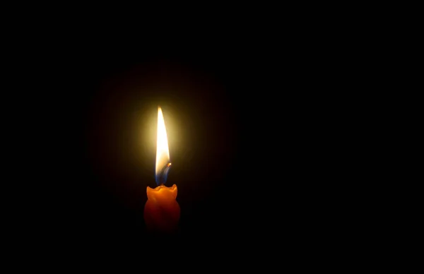 A single burning candle flame or light is glowing on spiral orange candle on black or dark background on table in church for Christmas, funeral or memorial service with copy space.