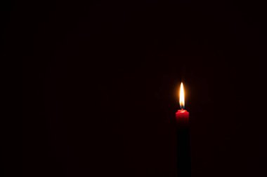 Tek bir yanan mum ya da ışık, kilisedeki Noel, cenaze ya da anma töreninde fotokopi alanı olan siyah ya da koyu arkaplanda küçük kırmızı bir mum üzerinde parlıyor..