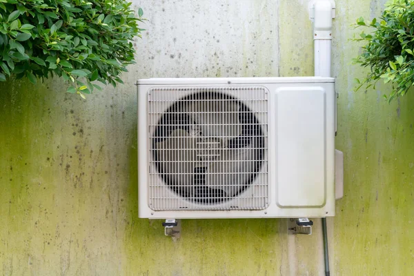 Air conditioner compressor outdoor unit is installed on dirty concrete wall outside the house or office.