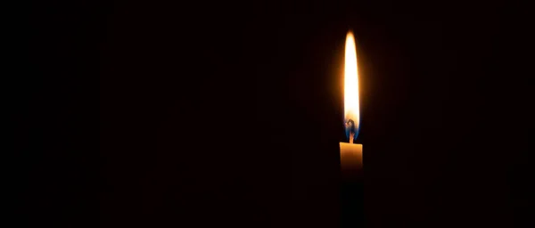 A single burning candle flame or light is glowing on a small orange candle on black or dark background on table in church for Christmas, funeral or memorial service with copy space