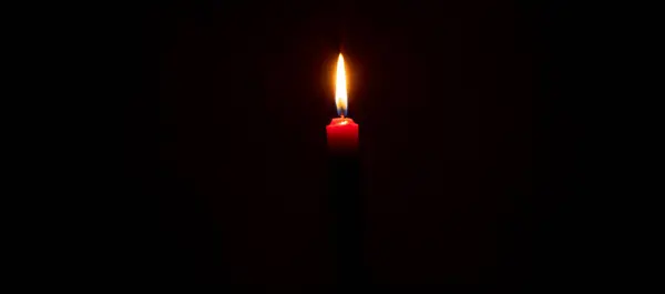 A single burning candle flame or light is glowing on red candle on black or dark background on table in church for Christmas, funeral or memorial service with copy space