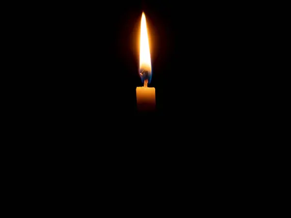 stock image A single burning candle flame or light is glowing on an orange candle on black or dark background on table in church for Christmas, funeral or memorial service with copy space