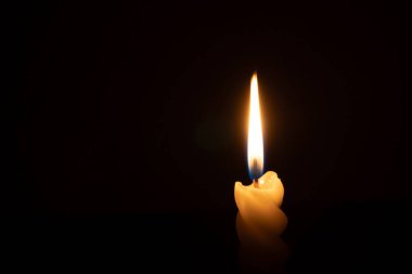Yanan tek bir mum ya da ışık, kilisede Noel, cenaze ya da anma töreninde fotokopi alanı olan siyah ya da koyu arkaplanda sarmal beyaz bir mum üzerinde parlıyor.