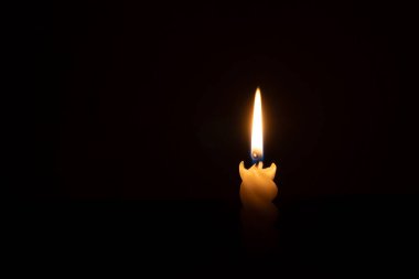 Yanan tek bir mum ya da ışık, kilisede Noel, cenaze ya da anma töreninde fotokopi alanı olan siyah ya da koyu arkaplanda sarmal beyaz bir mum üzerinde parlıyor.