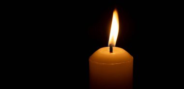 Büyük beyaz bir mumun üzerinde parlayan tek bir mum ya da ışık kilisedeki siyah ya da koyu arkaplanda Noel, cenaze ya da anma töreni için izole edilir.