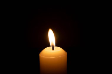 Büyük beyaz bir mumun üzerinde parlayan tek bir mum ya da ışık kilisedeki siyah ya da koyu arkaplanda Noel, cenaze ya da anma töreni için izole edilir.