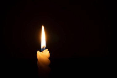 Yanan tek bir mum ya da ışık, kilisede Noel, cenaze ya da anma töreninde fotokopi alanı olan siyah ya da koyu arkaplanda sarmal beyaz bir mum üzerinde parlıyor.