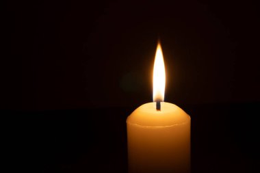 Büyük beyaz bir mumun üzerinde parlayan tek bir mum ya da ışık kilisedeki siyah ya da koyu arkaplanda Noel, cenaze ya da anma töreni için izole edilir.