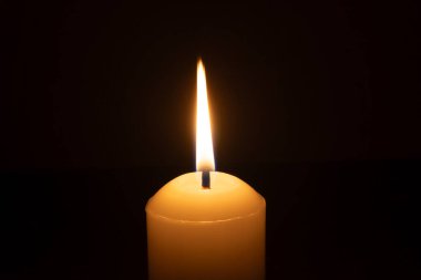 Büyük beyaz bir mumun üzerinde parlayan tek bir mum ya da ışık kilisedeki siyah ya da koyu arkaplanda Noel, cenaze ya da anma töreni için izole edilir.