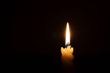 Yanan tek bir mum ya da ışık, kilisede Noel, cenaze ya da anma töreninde fotokopi alanı olan siyah ya da koyu arkaplanda sarmal beyaz bir mum üzerinde parlıyor.