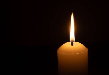 Büyük beyaz bir mumun üzerinde parlayan tek bir mum ya da ışık kilisedeki siyah ya da koyu arkaplanda Noel, cenaze ya da anma töreni için izole edilir.