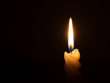 Yanan tek bir mum ya da ışık, kilisede Noel, cenaze ya da anma töreninde fotokopi alanı olan siyah ya da koyu arkaplanda sarmal beyaz bir mum üzerinde parlıyor.