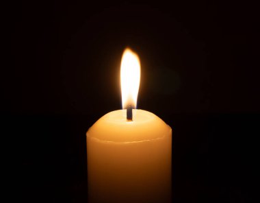 Büyük beyaz bir mumun üzerinde parlayan tek bir mum ya da ışık kilisedeki siyah ya da koyu arkaplanda Noel, cenaze ya da anma töreni için izole edilir.
