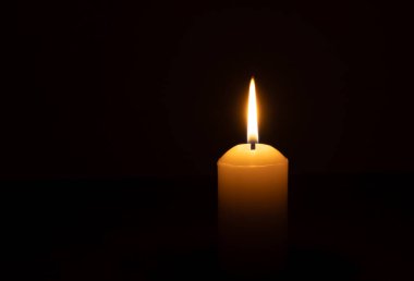 Büyük beyaz bir mumun üzerinde parlayan tek bir mum ya da ışık kilisedeki siyah ya da koyu arkaplanda Noel, cenaze ya da anma töreni için izole edilir.